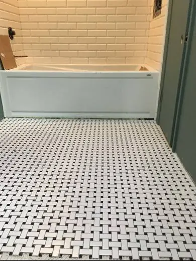 Black and white basketweave bathroom floor beside a subway tub surround