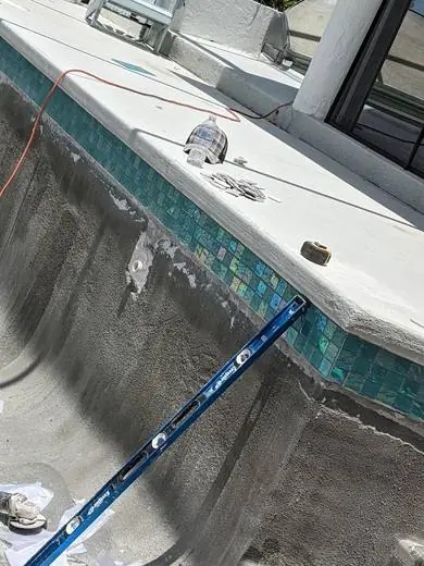 Teal glass waterline tile being set on a pool