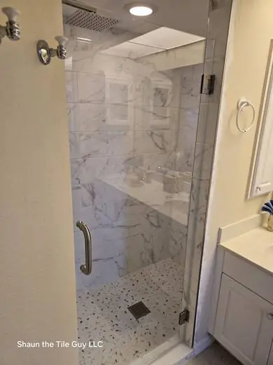 Frameless glass shower with a grab bar and marble-look walls
