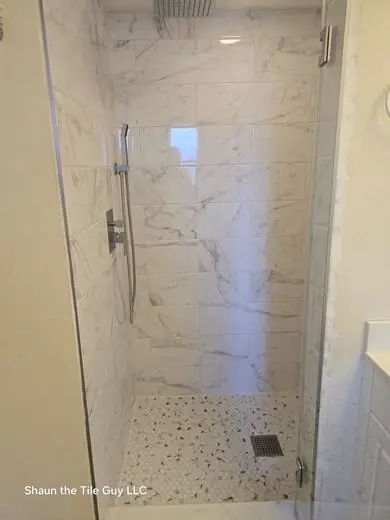 Finished marble-look shower with frameless glass and pebble floor