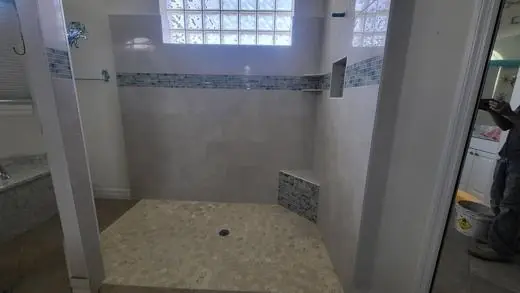Gray large-format shower with a glass-mosaic band and mosaic seat