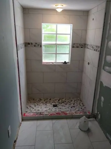 Marble-look shower with a pebble floor and accent band
