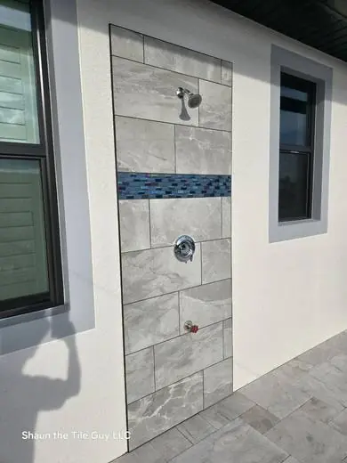 Outdoor shower wall in large-format gray tile with a blue glass accent