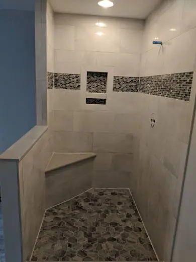 Travertine-look shower with a mosaic accent band and corner seat