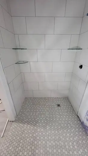Large-format white shower with glass shelves and a hex mosaic floor